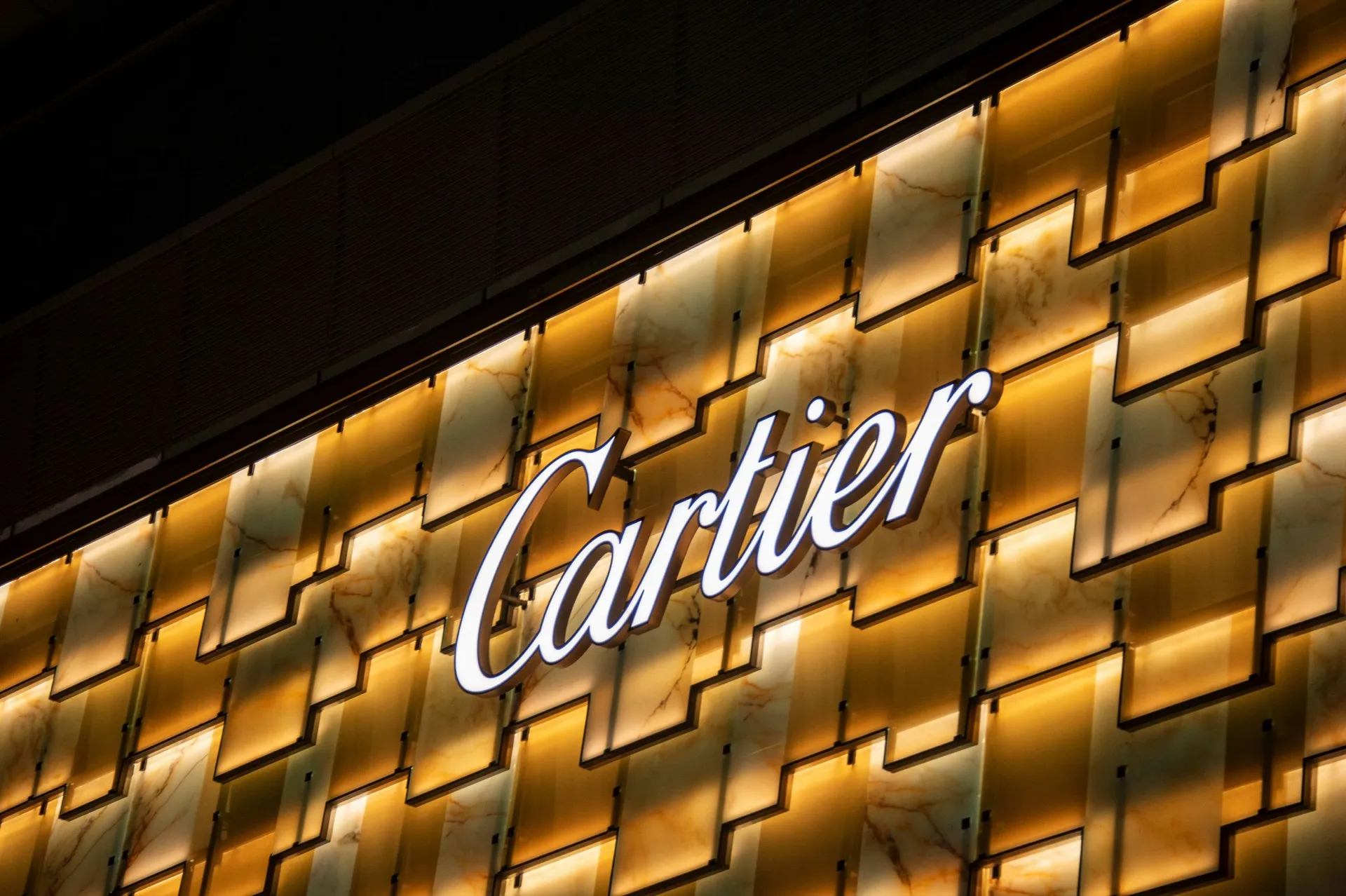 Illuminated Cartier boutique sign on marble facade at night