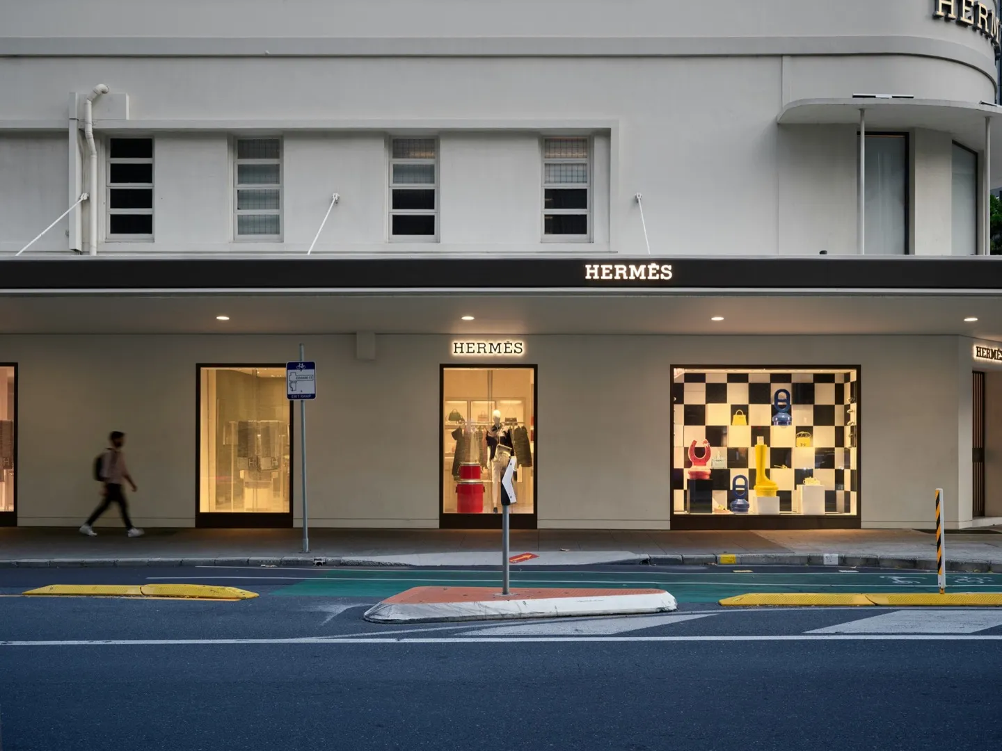 Hermès boutique storefront with illuminated signage and luxury window display featuring handbags