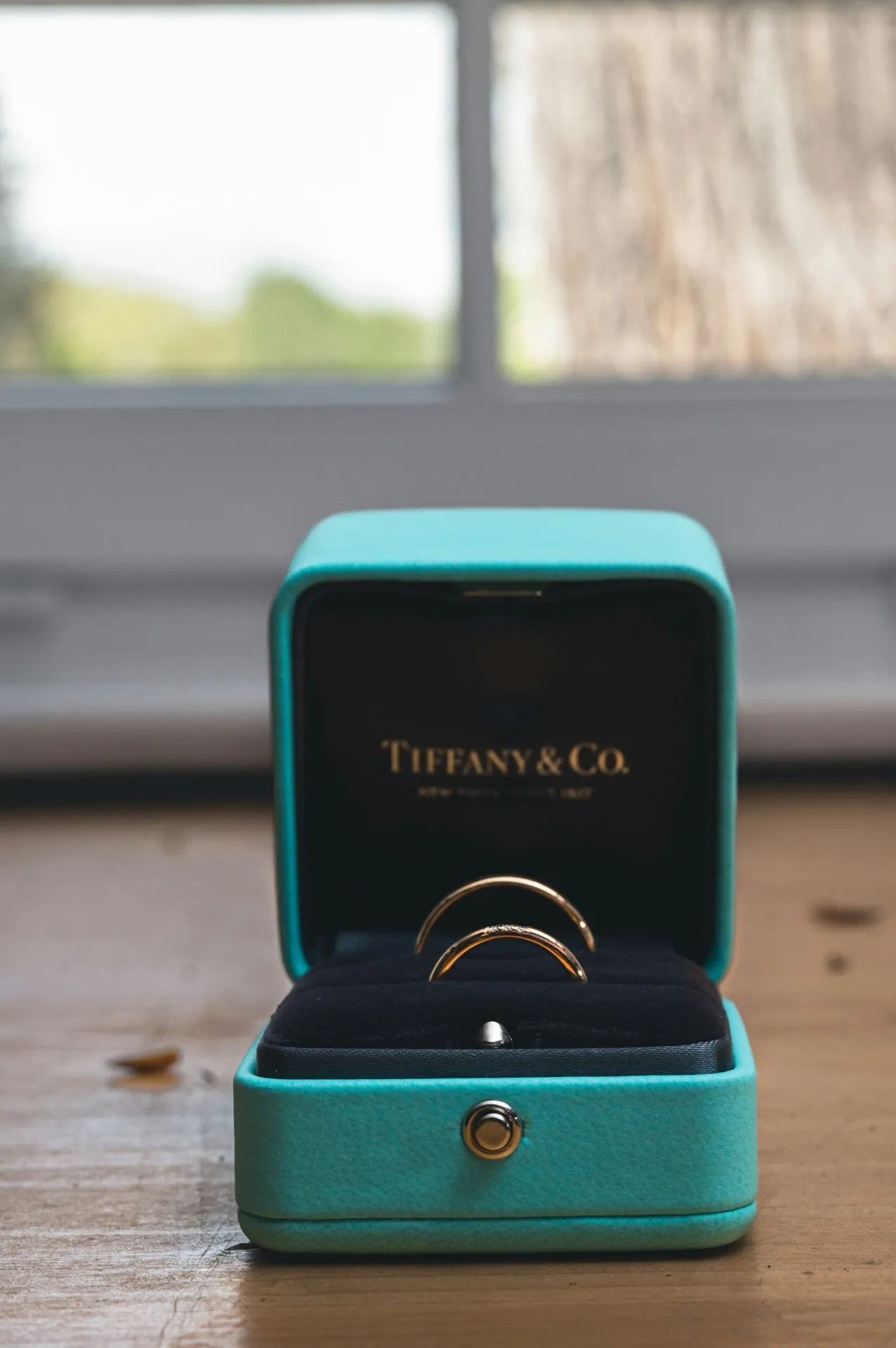 Two gold rings inside a Tiffany and Co. blue jewelry box on a wooden surface