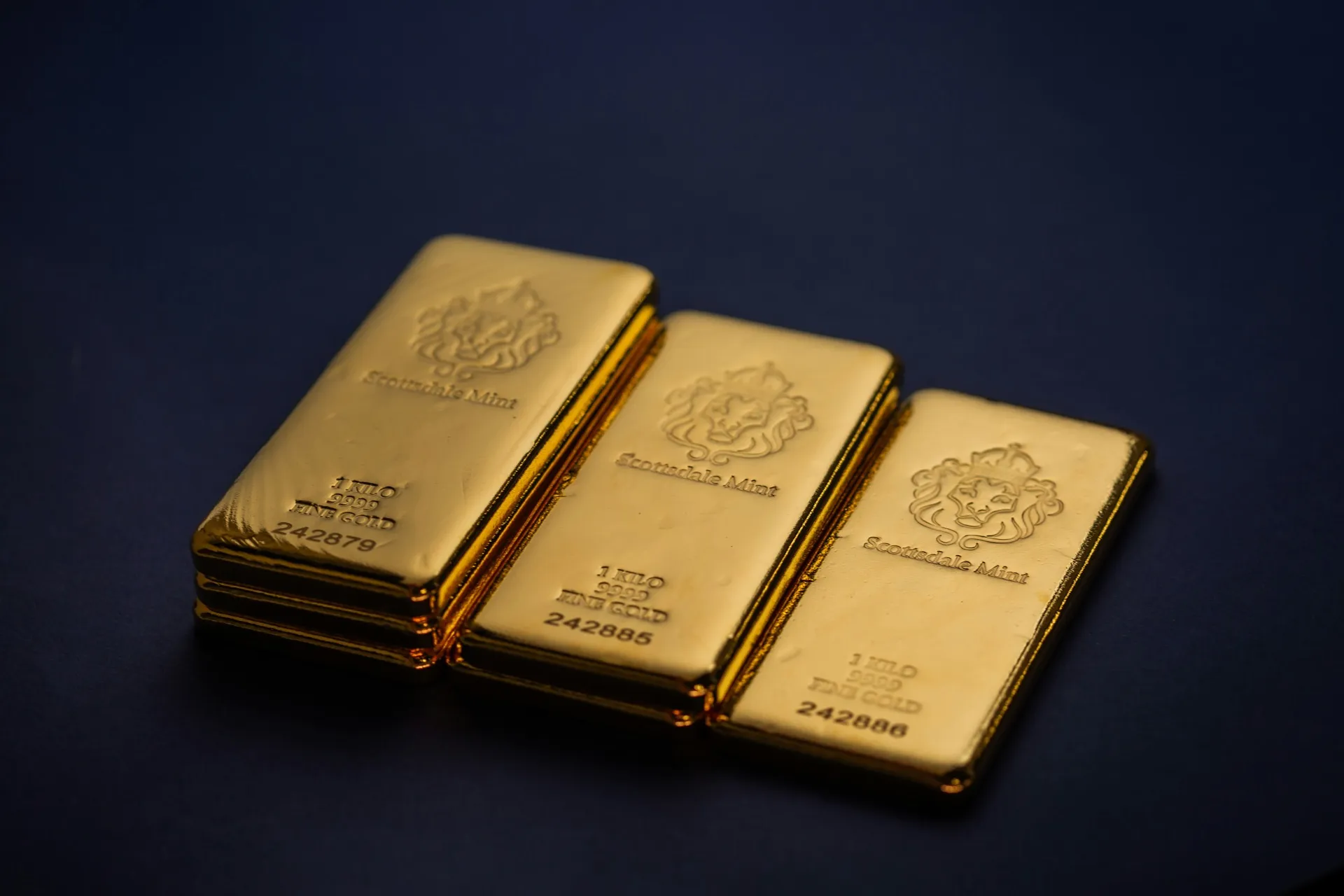Three 1-kilogram fine gold bars from Scottsdale Mint on dark background