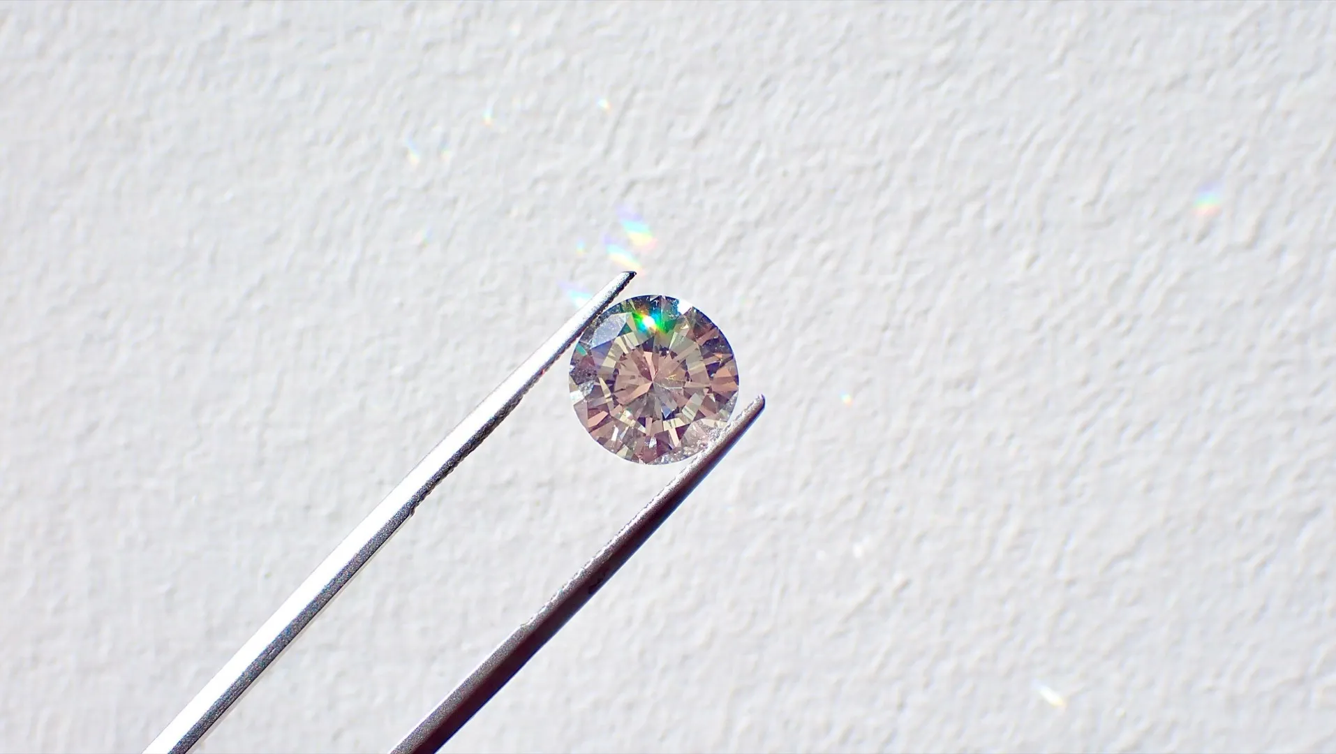 Champagne-colored diamond held in precision tweezers against white background showing cut and clarity