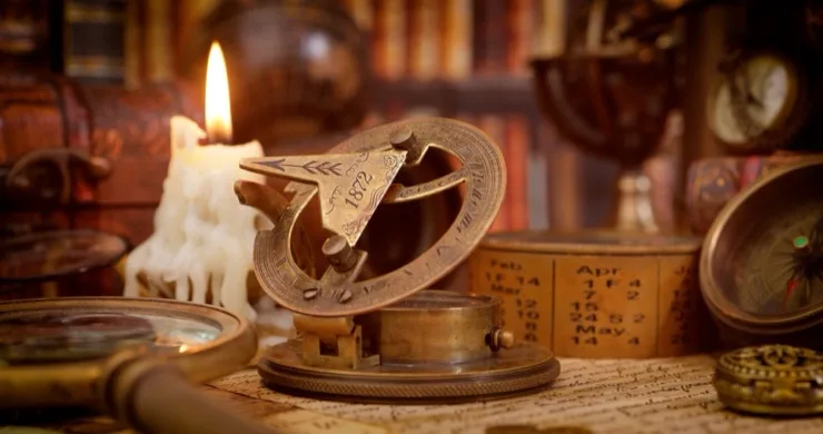 Vintage brass sundial compass surrounded by magnifying glass, candle, and old documents in a warm study