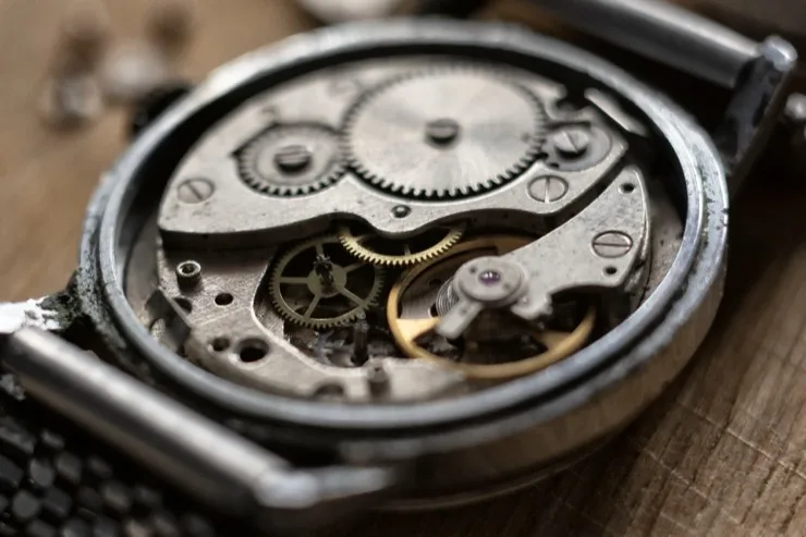 Open caseback of a mechanical watch showing intricate gears and movement on a wooden workbench