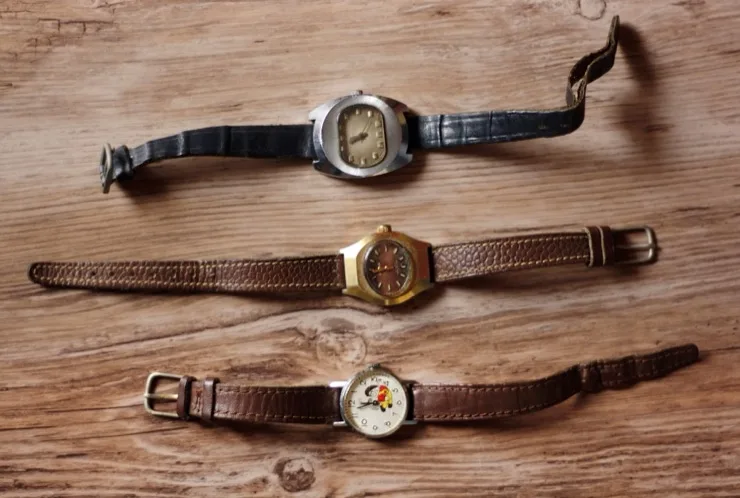 Three vintage wristwatches with leather straps laid flat on a rustic wooden surface